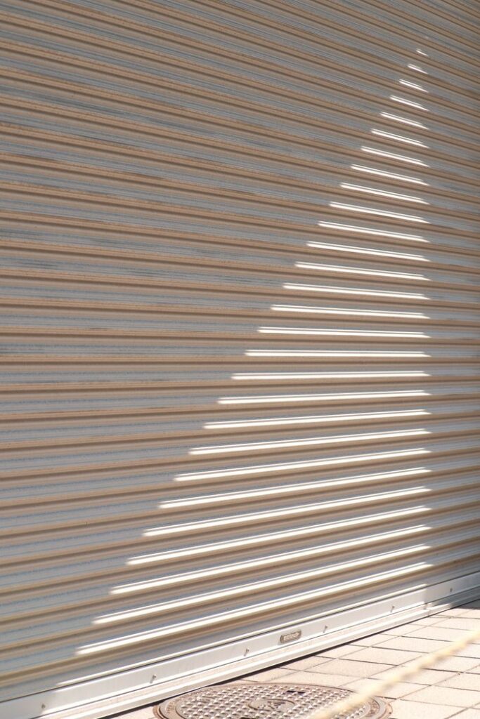 Abstract pattern of sunlight creating diagonal shadows on a corrugated metal shutter.